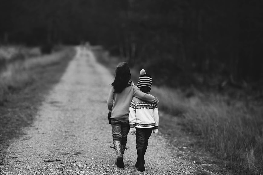 Two children walking away on a gravel road in black and white