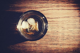 Top view of whiskey glass with ice cubes on wooden table