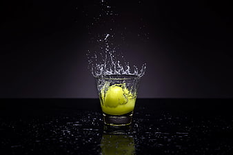 Tennis Ball Splashing into Shot Glass of Yellow Liquid