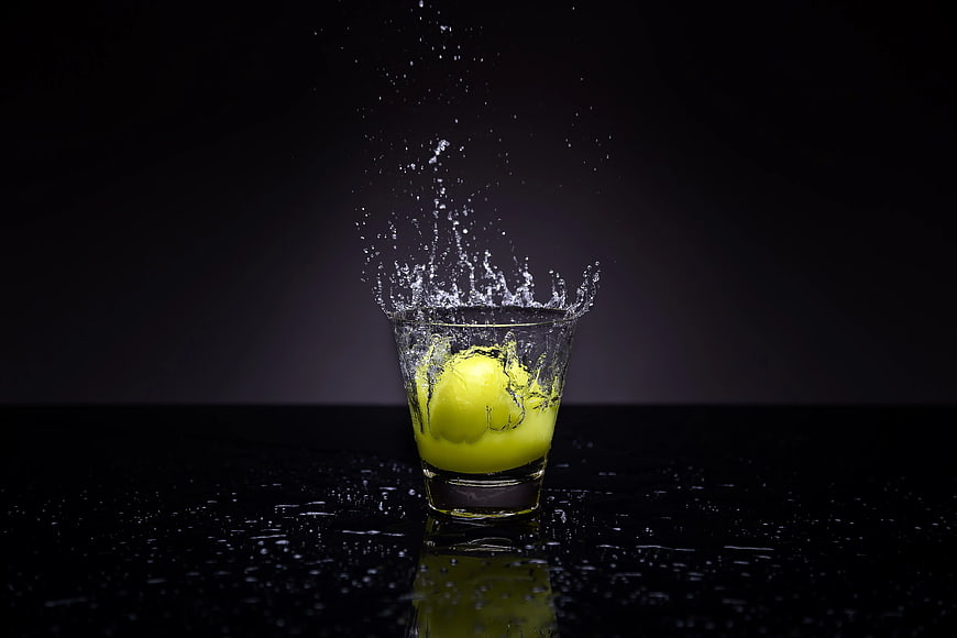 Tennis Ball Splashing into Shot Glass of Yellow Liquid