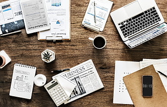 Top-down view of busy wooden office desk with laptop and documents