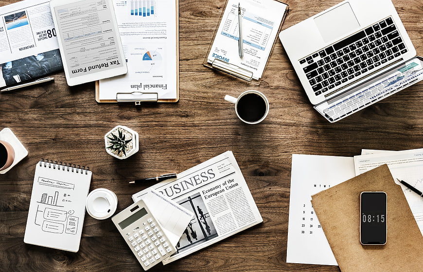 Top-down view of busy wooden office desk with laptop and documents