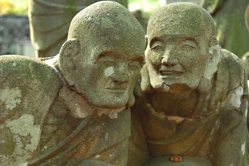 Two weathered stone monk statues conversing in a Japanese temple garden