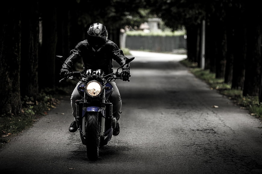 Motorcyclist riding down a dark tree-lined road