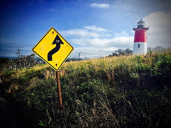 Yellow winding road sign with red and white lighthouse in background