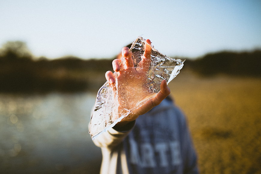 Hand holding translucent ice sheet against blurred nature background