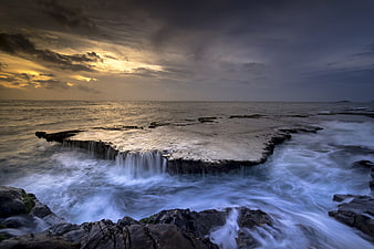 Dramatic Sunset Over Rocky Ocean Reef with Long Exposure Waves