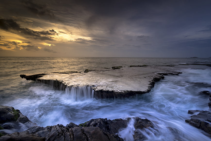 Dramatic Sunset Over Rocky Ocean Reef with Long Exposure Waves