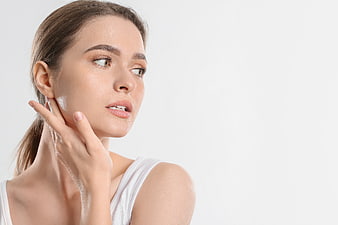 Woman touching face with cream against white background