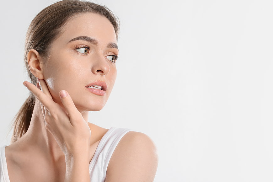 Woman touching face with cream against white background