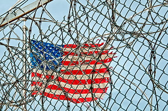American flag behind barbed wire fence and chain link