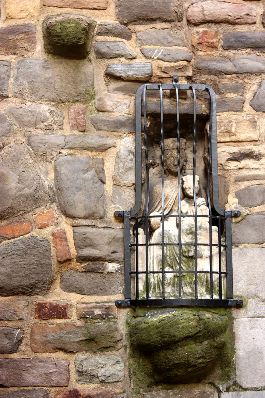 Ancient stone statue of Madonna and Child behind iron bars