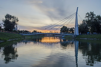 Modern cable-stayed bridge over river at sunset with reflections