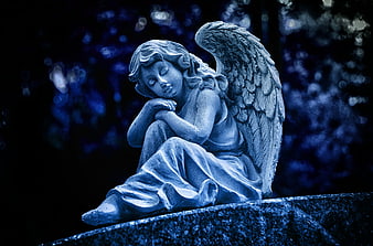 Blue Tinted Angel Statue Sitting On Stone At Night
