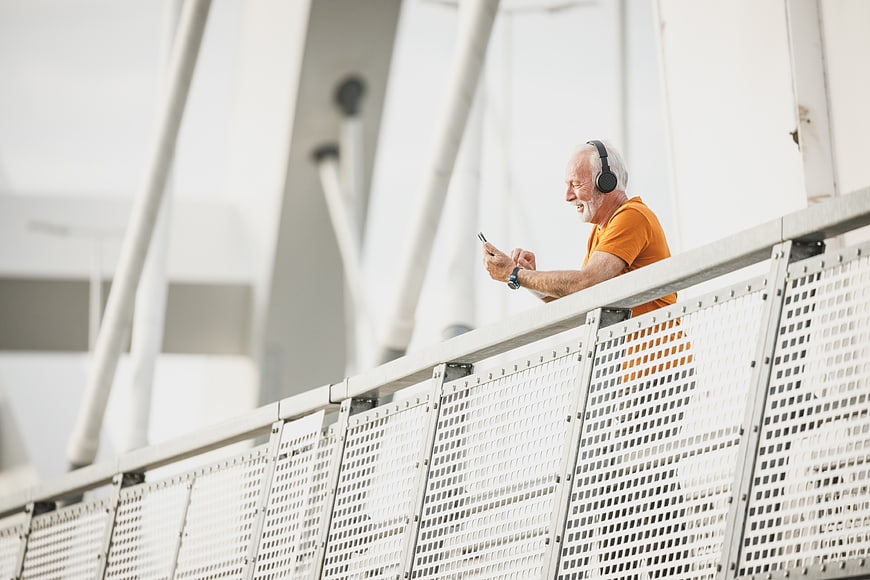 Happy Senior Man Listening to Music on Smartphone on Bridge