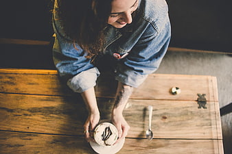 High angle view of woman holding cappuccino at rustic wooden table