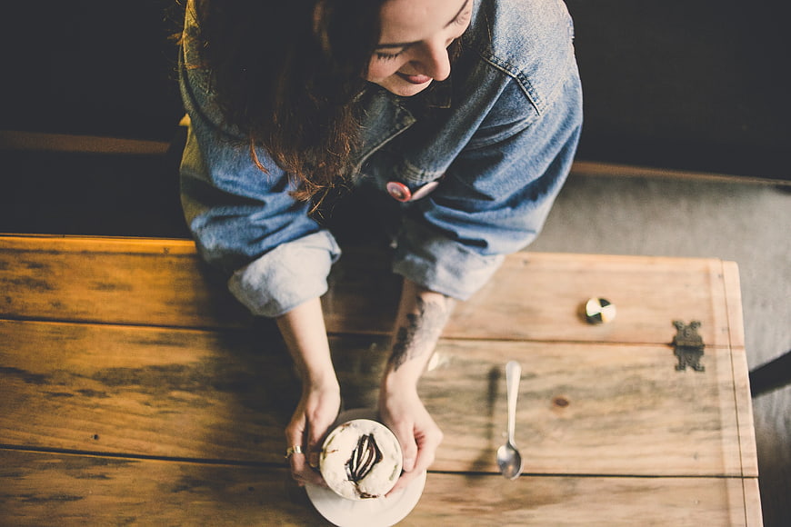 High angle view of woman holding cappuccino at rustic wooden table