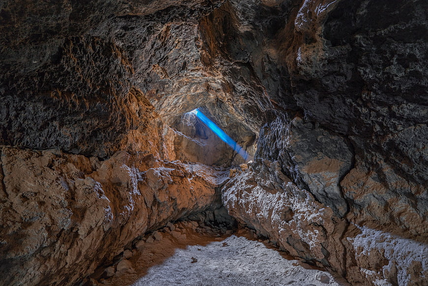 Dramatic blue sunbeam illuminating a rugged underground cave passage