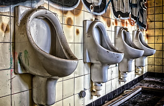 Dirty abandoned urinals in a graffiti-covered bathroom
