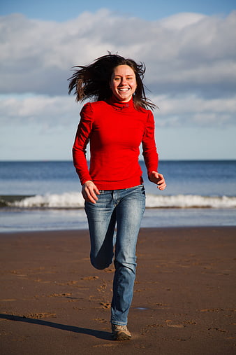 Happy Woman Running on Sandy Beach in Red Sweater