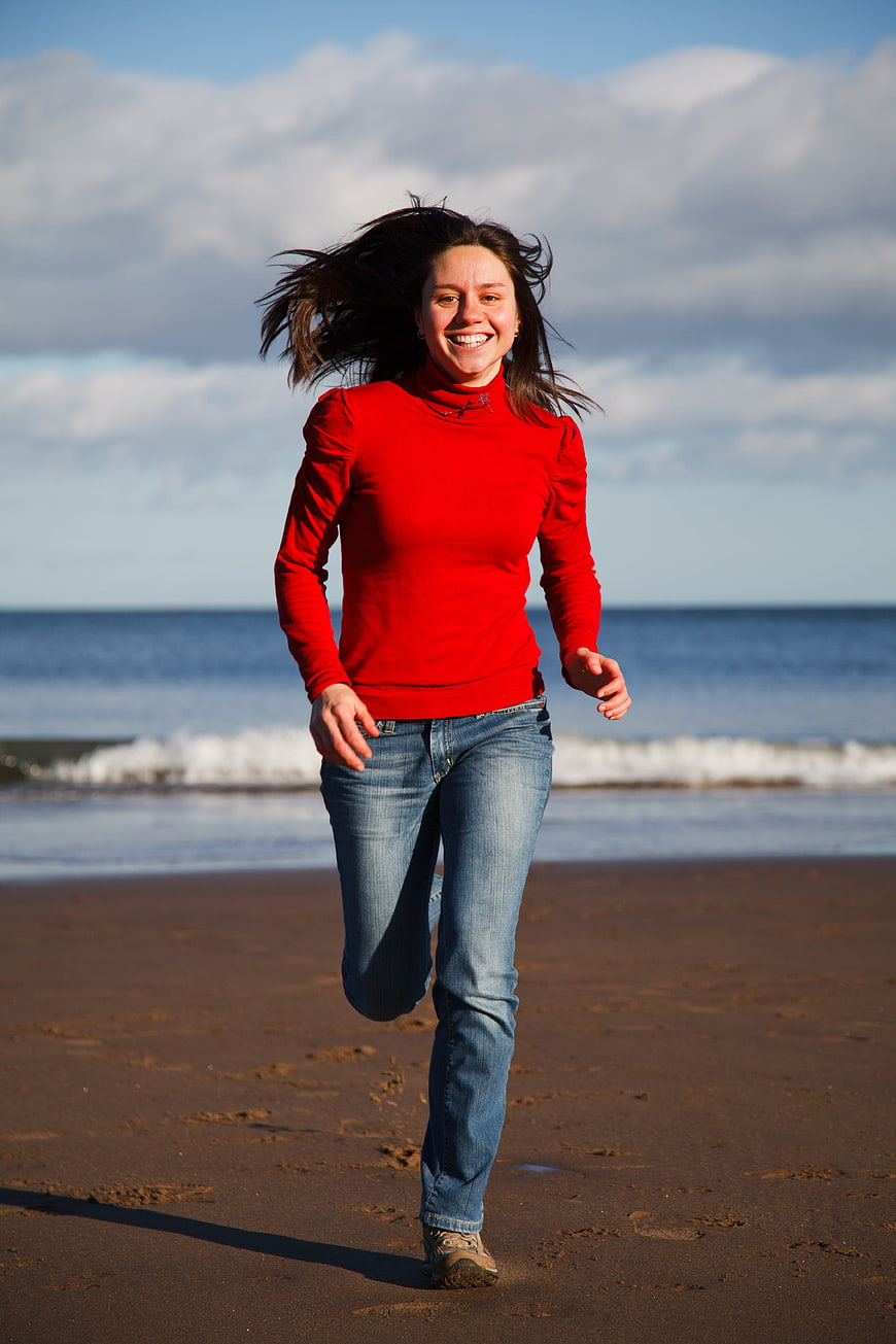 Happy Woman Running on Sandy Beach in Red Sweater