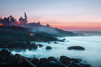 Misty coastal landscape at sunset with rocky shore and houses