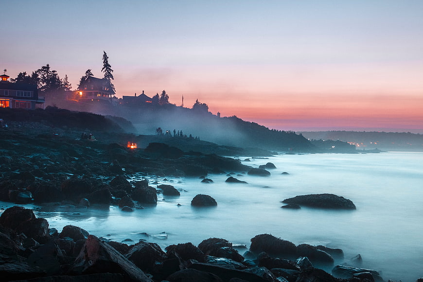 Misty coastal landscape at sunset with rocky shore and houses