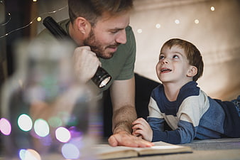 Father and son reading together with flashlight indoors