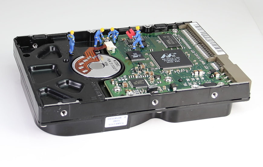 Miniature workers repairing open hard drive circuit board