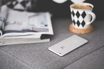 White smartphone on grey couch with coffee and magazine
