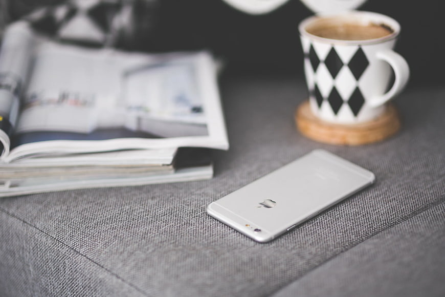White smartphone on grey couch with coffee and magazine