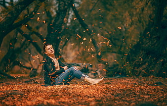 Man sitting in autumn forest with falling leaves