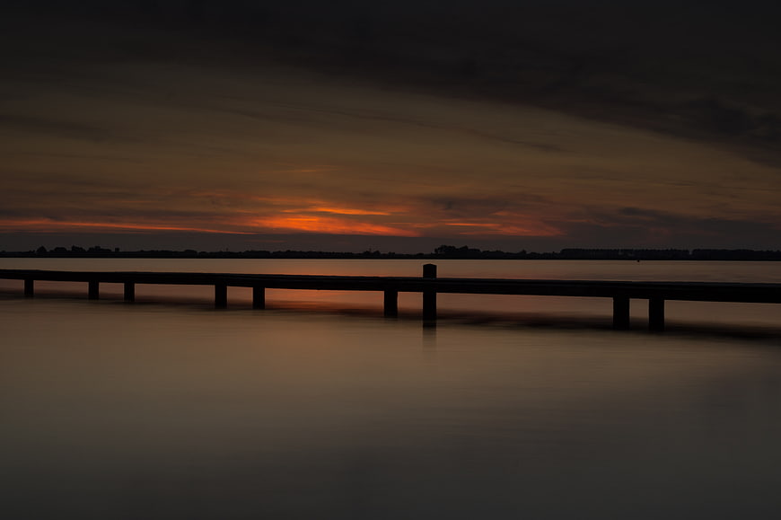 Silhouette of a pier at sunset over calm water