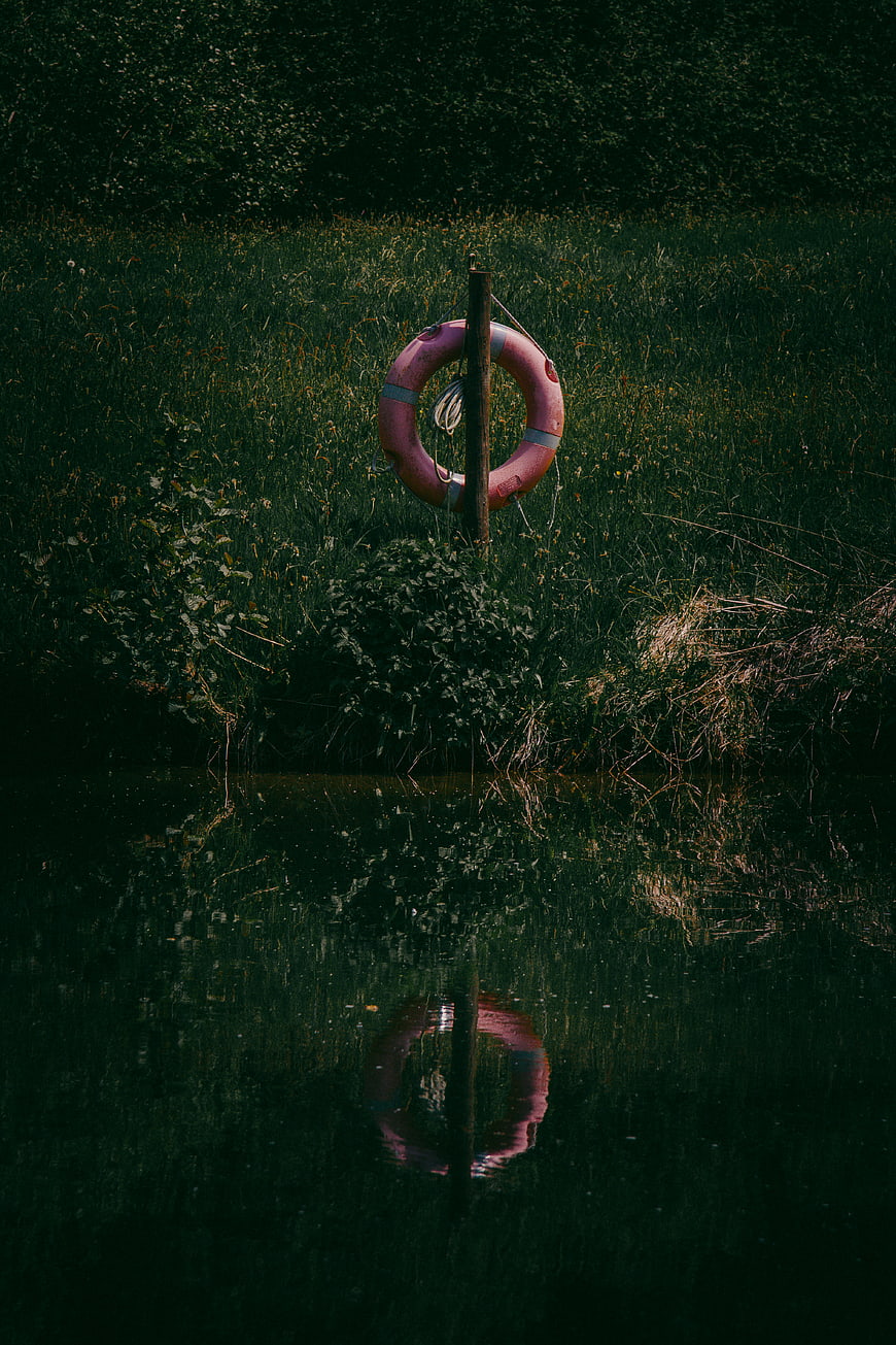 Pink Lifebuoy on Post by Dark River with Reflection