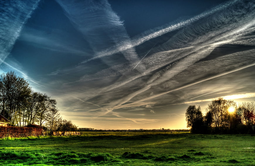 Dramatic Contrails in Blue Sky Over Green Pasture