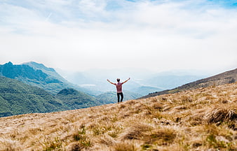 Man with arms raised on mountain summit overlooking valley
