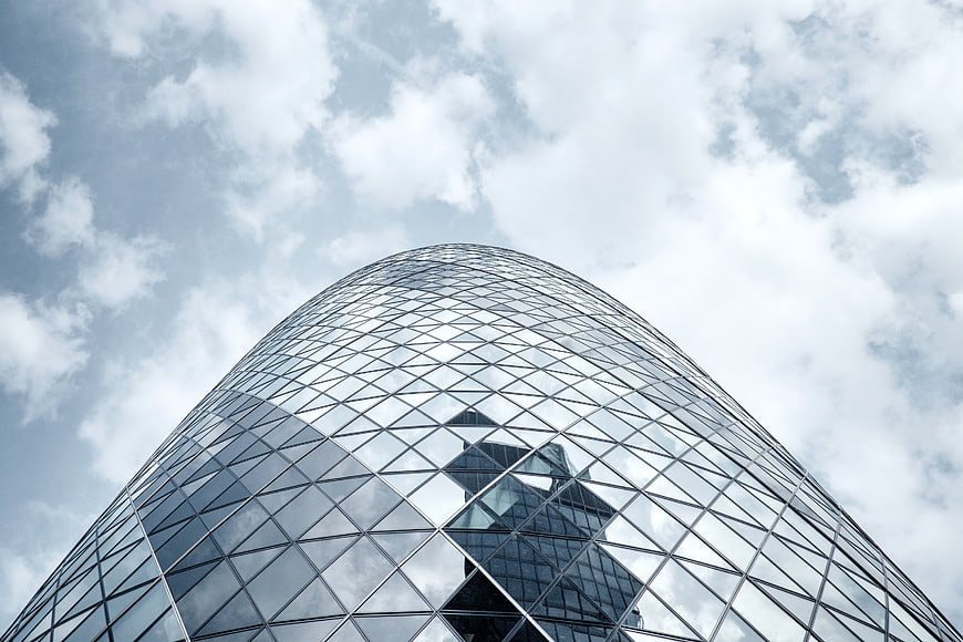 Low angle view of modern glass skyscraper reflecting clouds