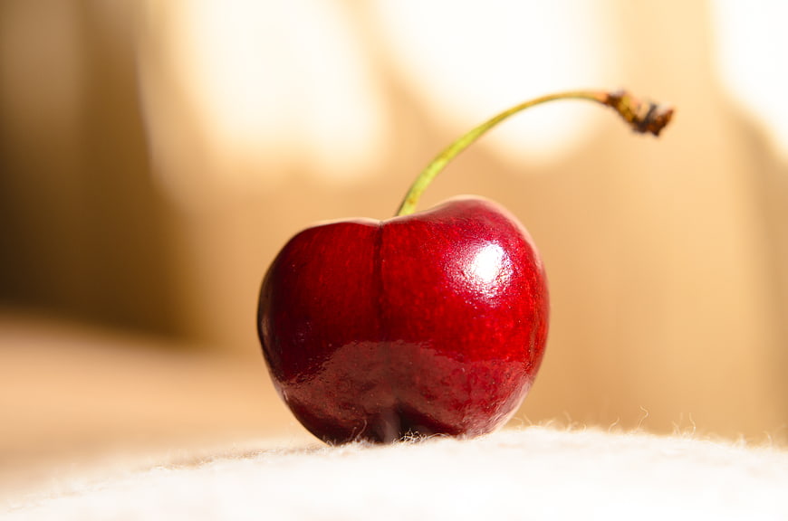 Close-up of a single ripe red cherry on a textured surface