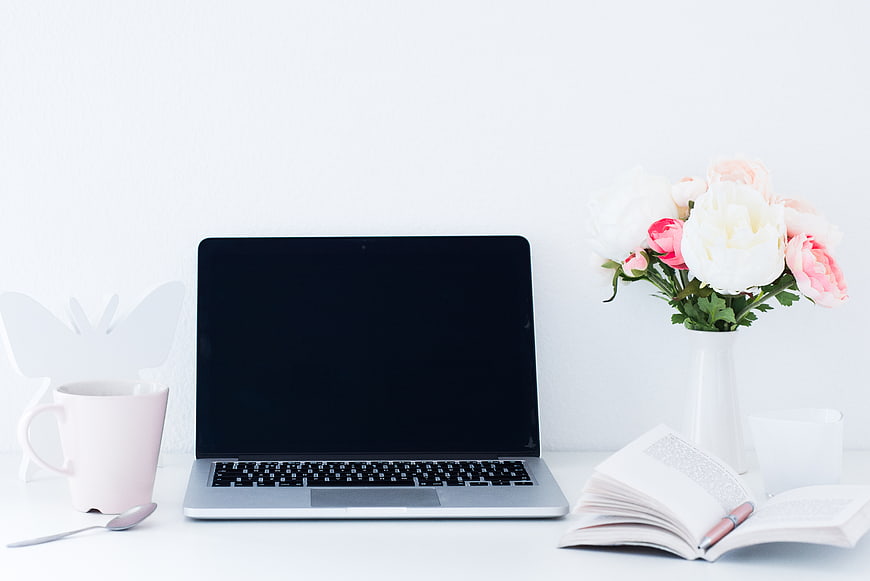 Minimalist white workspace with laptop, flowers, and book