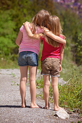 Two young girls hugging barefoot on a gravel path