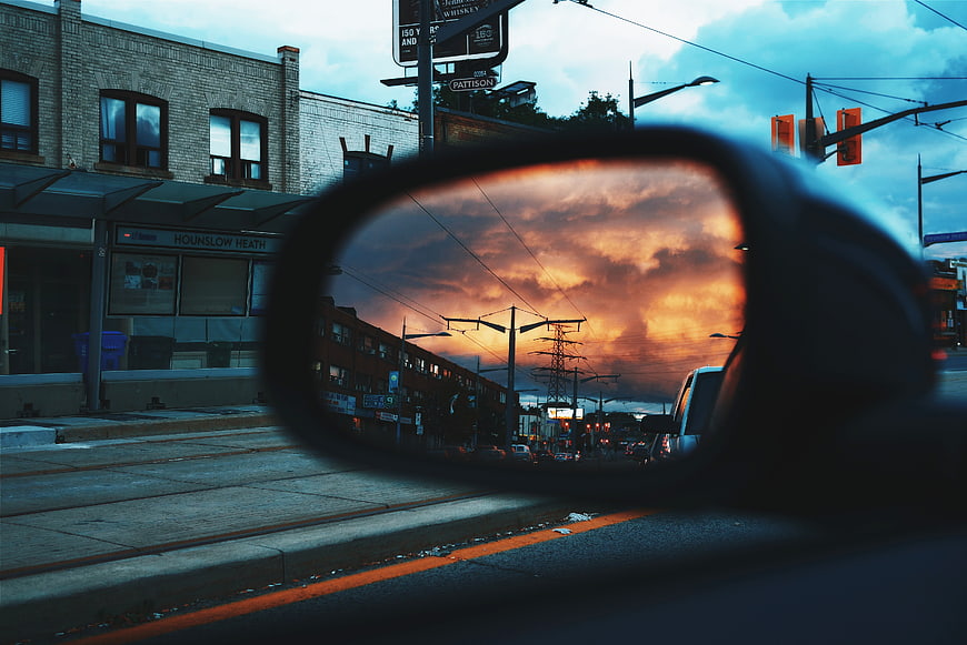 Dramatic sunset reflection in car side mirror on city street