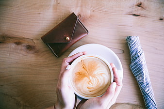 Top View of Hands Holding Cappuccino on Wooden Table