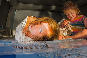 Two young children playing with a map and seashells in a car