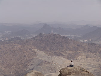 Man sitting on rocky mountain peak overlooking hazy desert valley and city