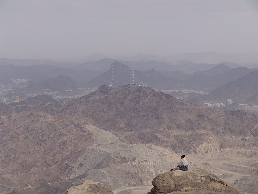 Man sitting on rocky mountain peak overlooking hazy desert valley and city