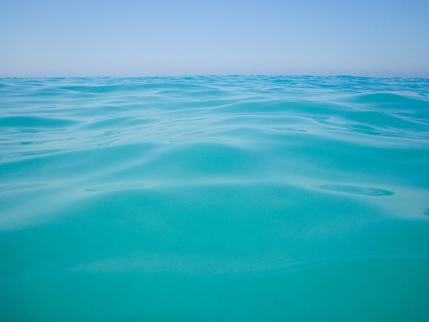 Abstract turquoise water surface with gentle ripples and blue sky