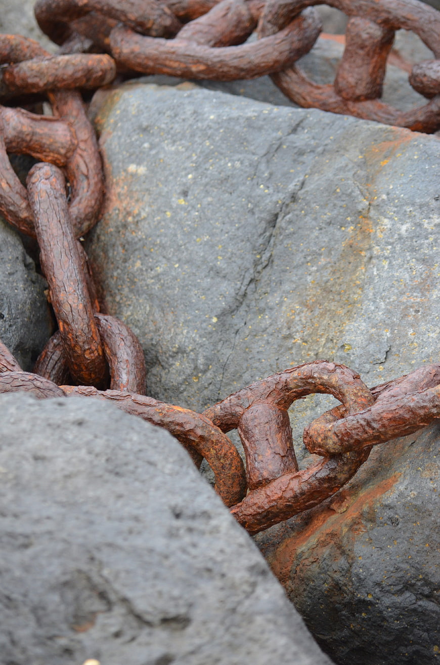 Close-up of heavy rusty iron chain on grey rocks