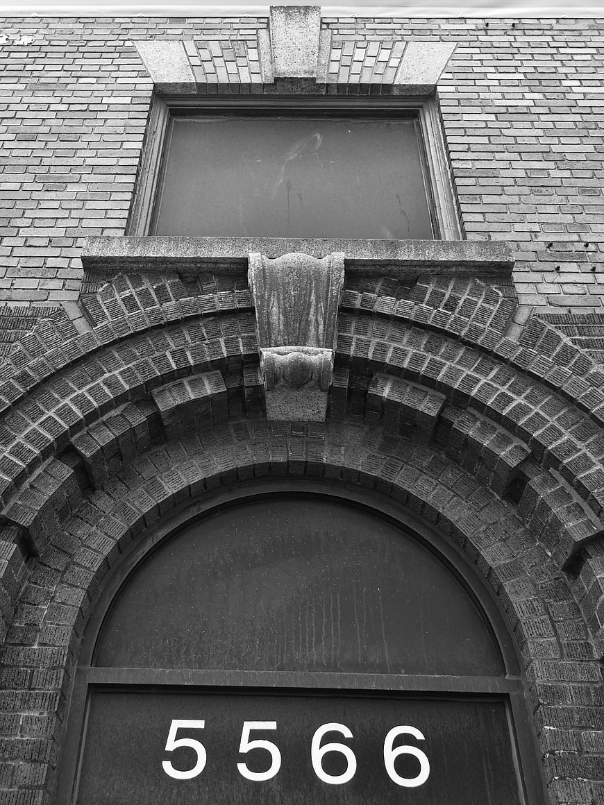 Black and white brick building facade with arched doorway and number 5566
