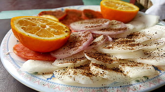 Sliced raw fish with spices, onions, and orange on a plate
