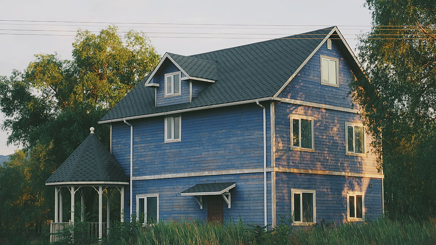 Blue wooden house with gazebo in overgrown garden